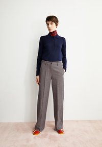 Marineblaues Langarm-Polohemd mit Knopfleiste, kombiniert mit hellgrauen weit geschnittenen Hosen und roten Schuhen. Glatter Stoff, klare Linien, lässiger Look.