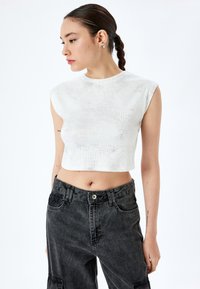 Vit cropped topp med ribbad yta och korta ärmar, i kombination med högmidjade svarta denim cargo-byxor med knapp- och fickdetaljer.