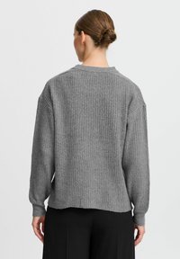Maglione a coste grigio con una vestibilità rilassata, maniche larghe e un orlo leggermente irregolare. Realizzato in un materiale morbido e texturizzato.