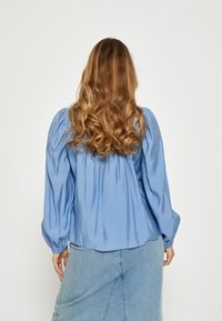 Hele sinine satiinsärgid, puffõlgadega, kogutud selja detailiga ja siledast tekstuurist, kombineeritud teksaseelikuga.