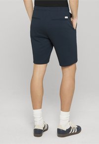 Shorts bleu marine en tissu doux avec une ceinture élastique, dotés de deux poches arrière et d'un détail étiquette. Design élégant et fonctionnel.