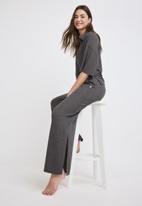 Graues geripptes Strick-Loungewear-Set mit einem locker sitzenden Oberteil und Schlaghosen, die seitliche Schlitze aufweisen, aus atmungsaktivem Material gefertigt.