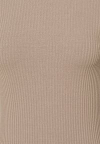 Haut en tricot côtelé beige, présentant un design ajusté avec une surface lisse et texturée ainsi que des lignes verticales subtiles.