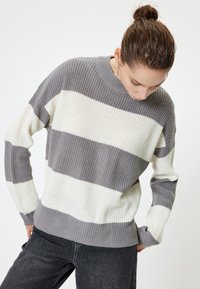 Grijze en witte gestreepte trui met een geribbelde textuur, ronde halslijn en lange mouwen. Draagt met donkere jeans.