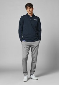 Marinblå långärmad polo med krage och logotyp, i kombination med grå joggerbyxor och vita sneakers. Avslappnad sportig stil.