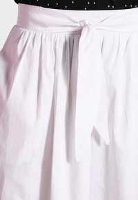 Gonna bianca in cotone con un design arricciato, dotata di una vita con nastro e una texture liscia. Silhouette semplice ed elegante senza fantasie.