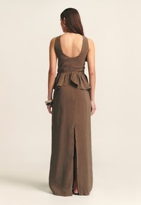 Ruskea peplum-mekko, jossa on syvä selkäaukko, pitkä helma ja sivuräjähtävyys. Pehmeä rakenne ja minimalistinen muotoilu, jossa on piilovetoketju.