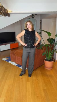 Black sequined sleeveless top paired with gray tailored trousers. Smooth texture, shiny embellishments, and a relaxed fit.
