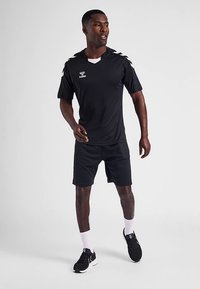 Svart sporttröja med korta ärmar, V-ringning och logotyp, kombinerad med svarta shorts, bärs med svarta sneakers och vita strumpor.