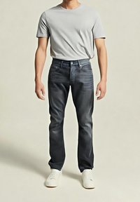 Šedé tričko v kombinaci s tmavě modrými d žíny s rovnými nohavicemi, jemným vyblednutím a designem s pěti kapsami. Bílé tenisky dotvářejí celkový vzhled.