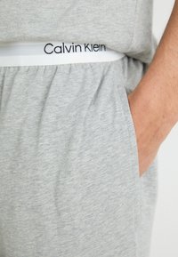 Grijze katoenen joggers met een zachte textuur, voorzien van een elastische tailleband met een witte band met daarop "Calvin Klein." Inclusief zijzak.