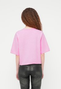 Πουλόβερ με κοντά μανίκια, κομμένο, ροζ, κατασκευασμένο από υφασμάτινο πλεκτό με υφή. Διαθέτει στρογγυλή λαιμόκοψη και ριμπ τελείωμα, συνδυασμένο με στενά μαύρα παντελόνια.