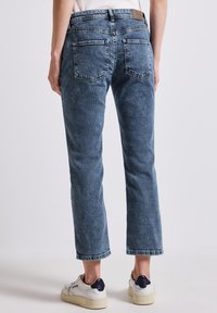 Hellblaue Jeans mit leicht abgenutzter Textur, geradem Schnitt und fransigem Saum. Vier Taschen und ein geprägtes Lederlabel auf der Rückseite.