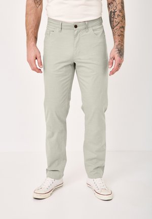 Man wearing light gray straight-fit pants and white sneakers, standing against a plain light background.