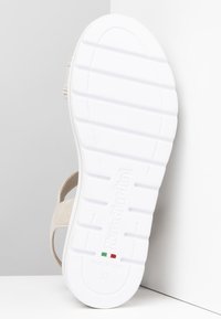 Sandalia beige con una suela de goma blanca texturizada, que presenta dos tiras anchas en el medio del pie. Marcada "Nero Giardini" y talla 37.
