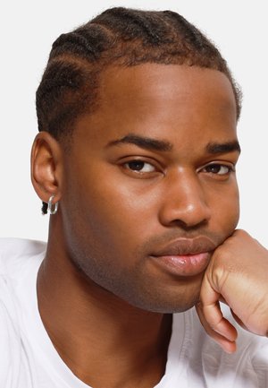 Jeune homme avec des cheveux courts et tressés, portant une boucle d'oreille en argent. Il repose son menton sur une main, avec une peau lisse et claire et une expression neutre.