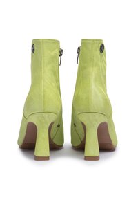 Botines de tacón alto en verde lima con una superficie texturizada, que cuentan con una cremallera trasera y un diseño de tacón curvado único.