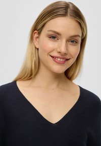 Marineblauer V-Ausschnitt-Pullover mit einem strukturierten Strickmuster. Das Material wirkt weich und hat einen entspannten Schnitt, der den Ausschnitt und den Schulterbereich betont.