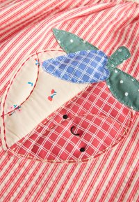 Patchwork de tela de un zorro sonriente con hojas verdes y una flor azul a cuadros sobre una tela a rayas rojas y blancas.