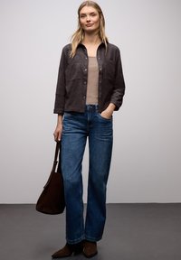 Sobrecamisa de ante marrón con botones, camiseta beige, vaqueros anchos azules, bolso de ante marrón y botines marrón oscuro. Textura suave, diseño minimalista.