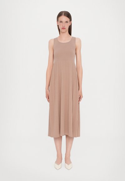 Ärmelloses Midi-Kleid aus beigem Rippstoff, mit einem enganliegenden Oberteil und einem fließenden Rock. Kombiniert mit weißen spitzen Absatzschuhen.