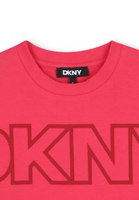 Camiseta de algodón rosa con cuello redondo y logotipo de DKNY en un tono más oscuro. Textura suave con mangas cortas.