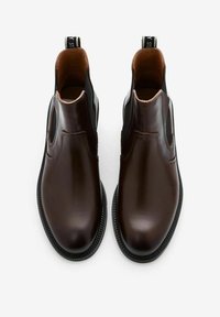 Een paar donkerbruine leren Chelsea-boots met zwarte elastische zijkanten en instaplussen aan de achterkant, van bovenaf weergegeven op een witte achtergrond.