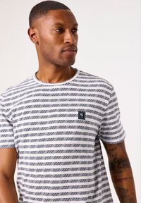 Camiseta a rayas con rayas horizontales en azul marino y blanco, escote redondo y un pequeño parche de logo. Mangas cortas y material de algodón.