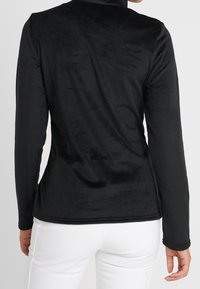 Top negro de manga larga hecho de una tela suave y texturizada, con un cuello alto y un corte ajustado, exhibido sobre un fondo neutro.