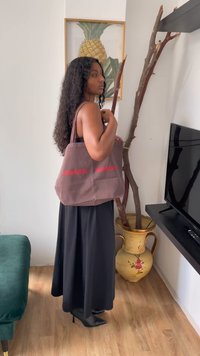 Καφέ καμβάς τσάντα με κόκκινο κείμενο "SAM SøE", με ανθεκτικές λαβές και ορθογώνιο σχήμα, κρατούμενη από ένα άτομο που φοράει μαύρη μακριά φούστα.