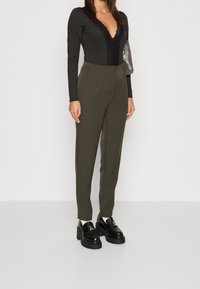 Svart långärmad bodysuit med spetsdetaljer, i kombination med högmidjade olivgröna byxor och kraftiga svarta plattformsskor. Silverfärgad handväska som accent.