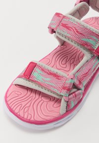 Róžinės šlepetės su tekstūruotais diržais, turinčiais bangų tipo raštą. Velcro užsegimai ir paminkštintas, kontūruotas padas. Guminis padas.