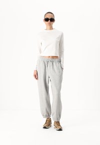 Balta ilga rankovė crop top'as su pilkais sportiniais džinsais. Kelnės turi elastinę liemenę ir elastines rankoves. Rudos sportbačiai užbaigia aprangą.