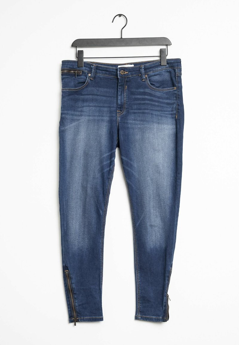 Jeans skinny en denim bleu foncé, avec des poches avant, une fermeture éclair et des accents zippés au niveau de la cheville. Texture lisse avec des détails décolorés.