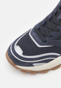 Baskets bleu marine avec une tige en mesh, des accents en daim, une semelle en caoutchouc, un embout rond et des détails contrastés en blanc et gris.