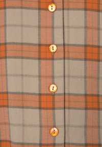 Flanellhemd mit einem beigen und orangefarbenen Karomuster, das orangefarbene Knöpfe und graue Akzentlinien entlang der Quadrate aufweist.