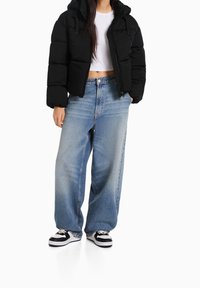 Černá péřová bunda s krátkým střihem, spárovaná s volnými světle modrými džíny. Boty mají černobílé barevné blokování.