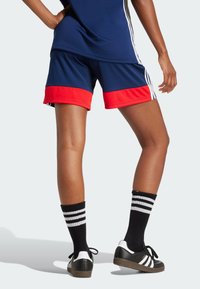 Marineblauwe sportshorts met een rode band aan de zoom, zijstrepen en zwarte sokken met witte strepen, gecombineerd met zwarte sneakers.