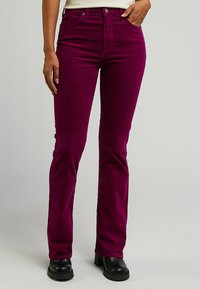 Flared corduroy broek in diep magenta, met een zachte textuur, een knoop- en ritssluiting, en voorzakken, gecombineerd met zwarte platformlaarzen.