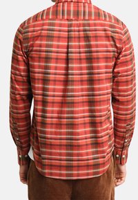 Camicia a quadri rossa e marrone con maniche lunghe, polsini abbottonati e un dettaglio di spalla sul retro, realizzata in tessuto strutturato.