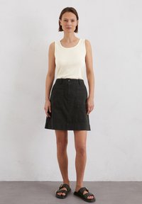 Witte geribbelde tanktop, donkergroene A-lijn rok met zakken, en platte zwarte sandalen met gouden accenten. Zacht katoenmateriaal, casual ontwerp.