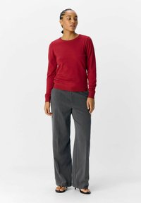 Pull rouge à manches longues avec un col rond, associé à un pantalon large gris, en tissu texturé et au design minimaliste.