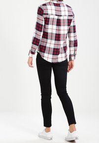 Rutig skjorta i rött, navy och vitt med lång ärm, knappärmar och en rundad nederkant. Bärs över svarta skinny jeans och vita sneakers.