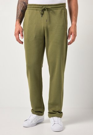 Man draagt olijfgroene joggingbroek met elastische tailleband met trekkoord en witte sneakers tegen een effen achtergrond.