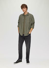 Groen en grijs geruite overhemd over een donkergroen t-shirt, gedragen met zwarte jeans en zwarte sneakers met witte zolen.