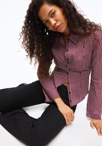 Vinröd och vit randig skjorta med knappar, långärmad med en lätt utställd design, kombinerad med svarta figurnära byxor.