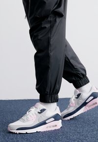 Zapatillas deportivas blancas y grises con acentos en rosa y azul marino. Diseño de cordones, cuello acolchado y amortiguación de aire visible en la suela.