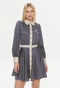 Abito a fantasia navy con colletto e bottoni bianchi, maniche lunghe, vita affusolata e gonna svasata; presenta un motivo a fiocco ripetuto.
