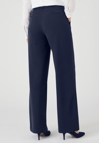 Marineblauwe, wijde broek met zijzakken en achterzakken met paspel, gemaakt van een gladde stof, gecombineerd met blauwe stilettohakken.