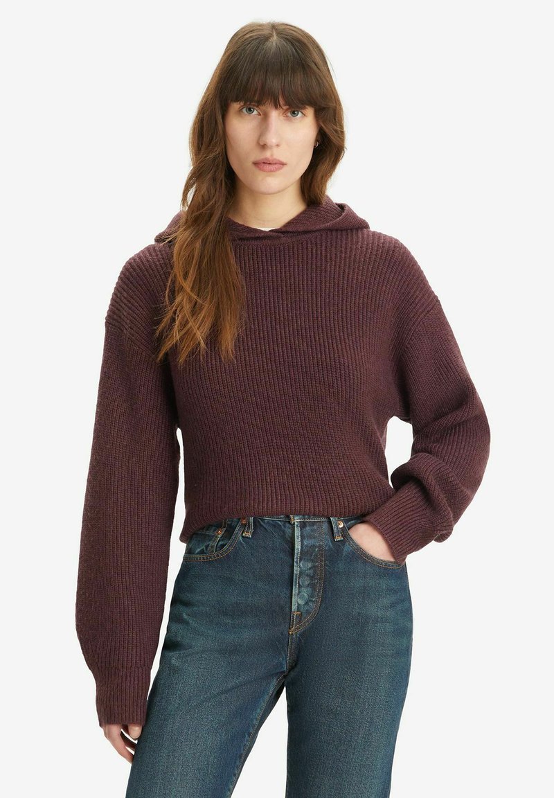 Burgundy Strickhoodie mit gerippter Textur, lässiger Passform und langen Ärmeln, kombiniert mit hoch taillierten blauen Jeans.